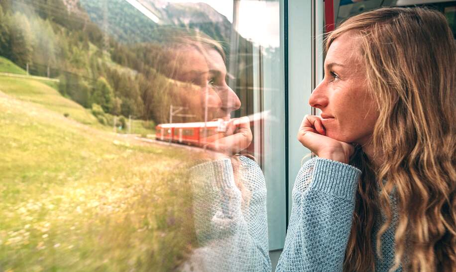 Frau, die mit dem Zug aus dem Fenster schaut und die landschaftlich vorbeifahrende Landschaft geniesst | © Gettyimages.com/Mystockimgaes