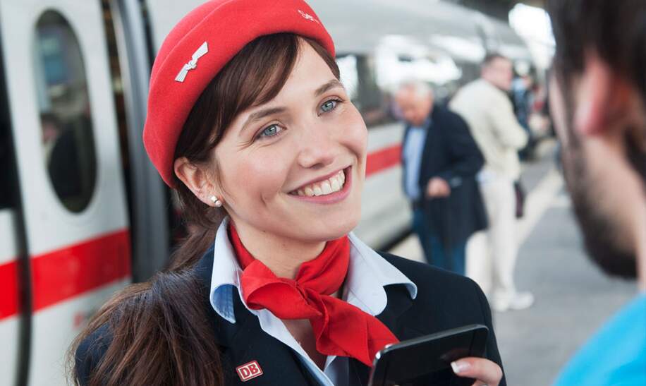  Schaffnerin mit roter Mütze und Schal, die versucht, einem Reisenden mit ihrem mobilen Gerät zu helfen | © Deutsche Bahn AG