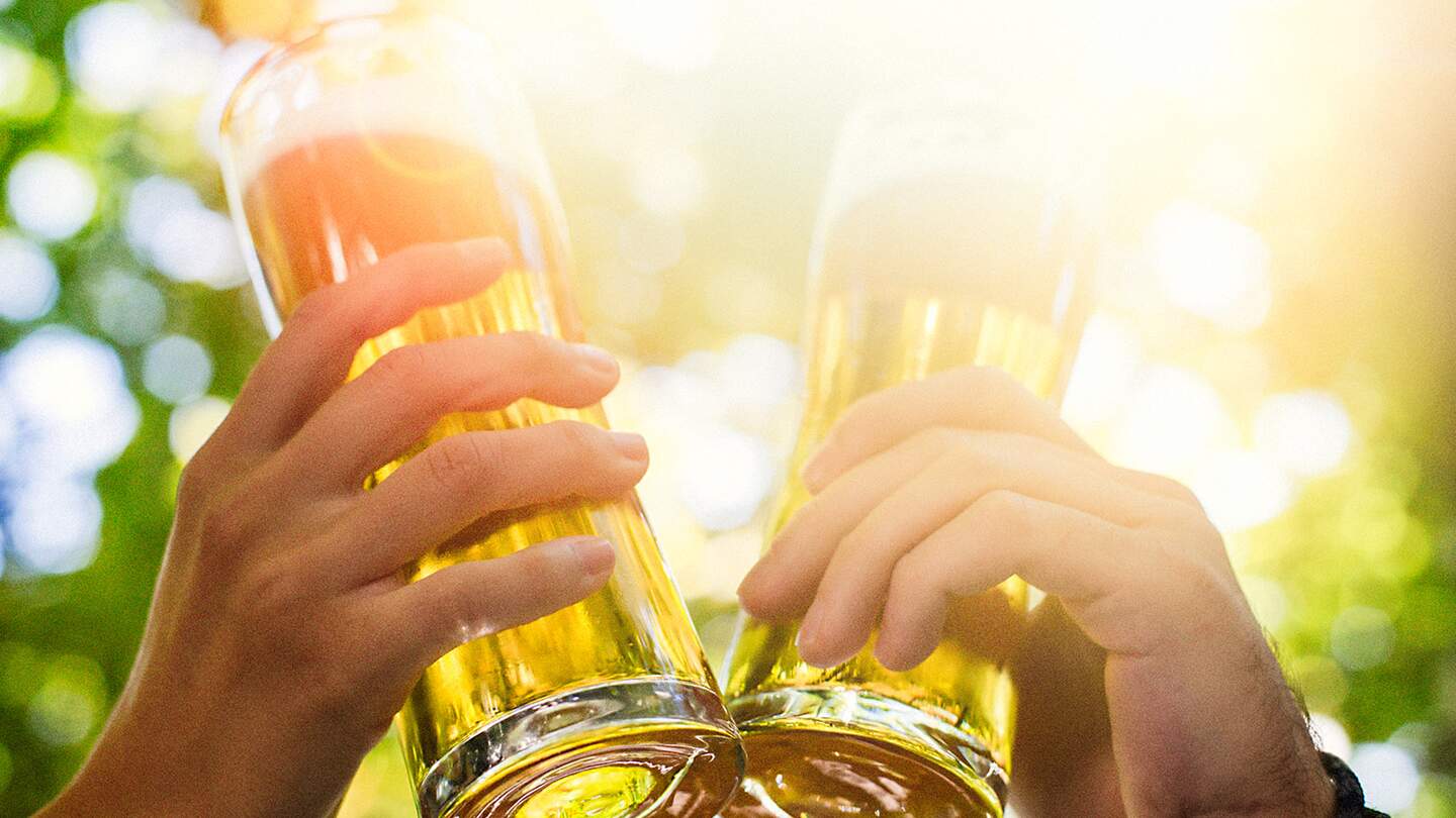 Zwei Personen stossen mit Bierglaesern im Biergarten an | © Gettyimages.com/suteishi