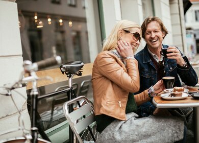 Paar trinkt Kaffe und ist Kuchen an einem Tisch im Aßenbereich eines Cafès | © Gettyimages.com/Geber86