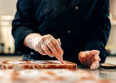 Nahaufnahme der Hände eines Konditors, der weiße Pralinen in einer handwerklichen Werkstatt schmückt, Brüssel | © Gettyimages.com/Carlo Prearo