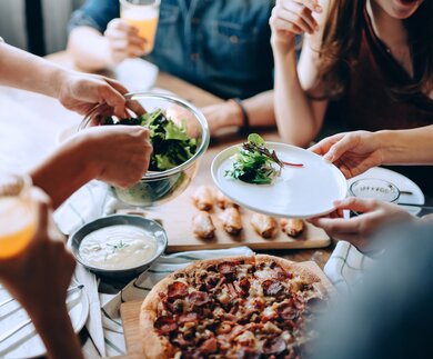 Nahaufnahme einer jungen Gruppe fröhlicher Freunde, die Spaß daran haben, zusammen zu genießen, Essen über den Esstisch auf der Party zu verteilen und zu teilen | © Gettyimages.com/AsiaVision