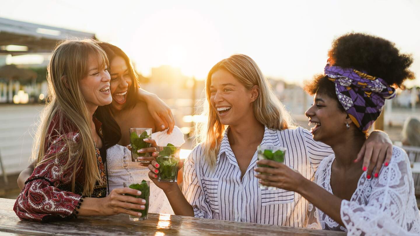 Glückliche Mädchen, die Spaß daran haben, Cocktails an der Bar am Strand zu trinken | © Gettyimages.com/disobeyart