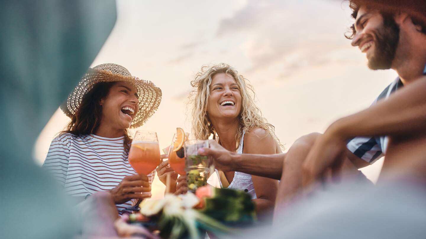 Niedrige Winkelansicht von glücklichen Frauen, die mit ihrem männlichen Freund am Sommertag anstoßen. | © Gettyimages.com/skynesher