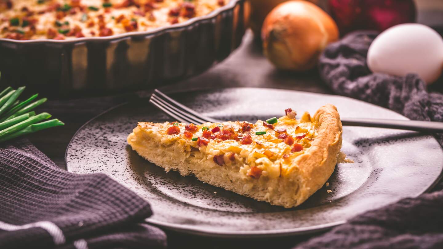 Stueck hausgemachter Zwiebelkuchen mit Speck und Schnittlauch auf Holzhintergrund | © Gettyimages.com/brebca