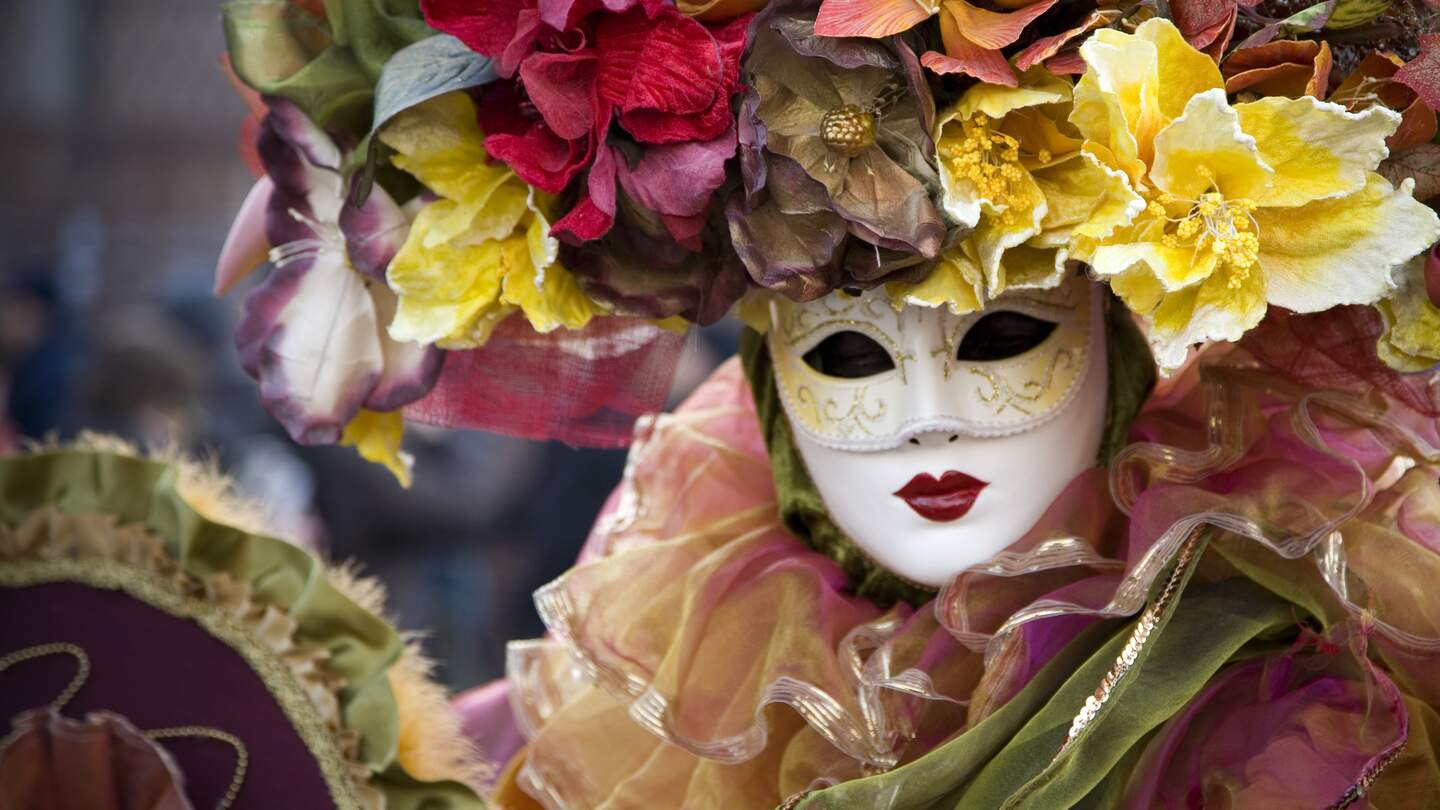 Frau in venezianischer Karnevals Verkleidung, mit Maske, pompösem Blumenkopfschmuck und vielen Rüschen | © GettyImages.com/t-lorien