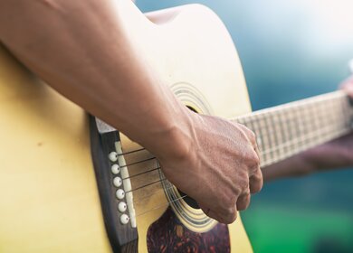 Nahaufnahme eines Gitarrenspielers mit Fokus auf die Gitarre | © Gettyimages.com/ChatkarenStudio