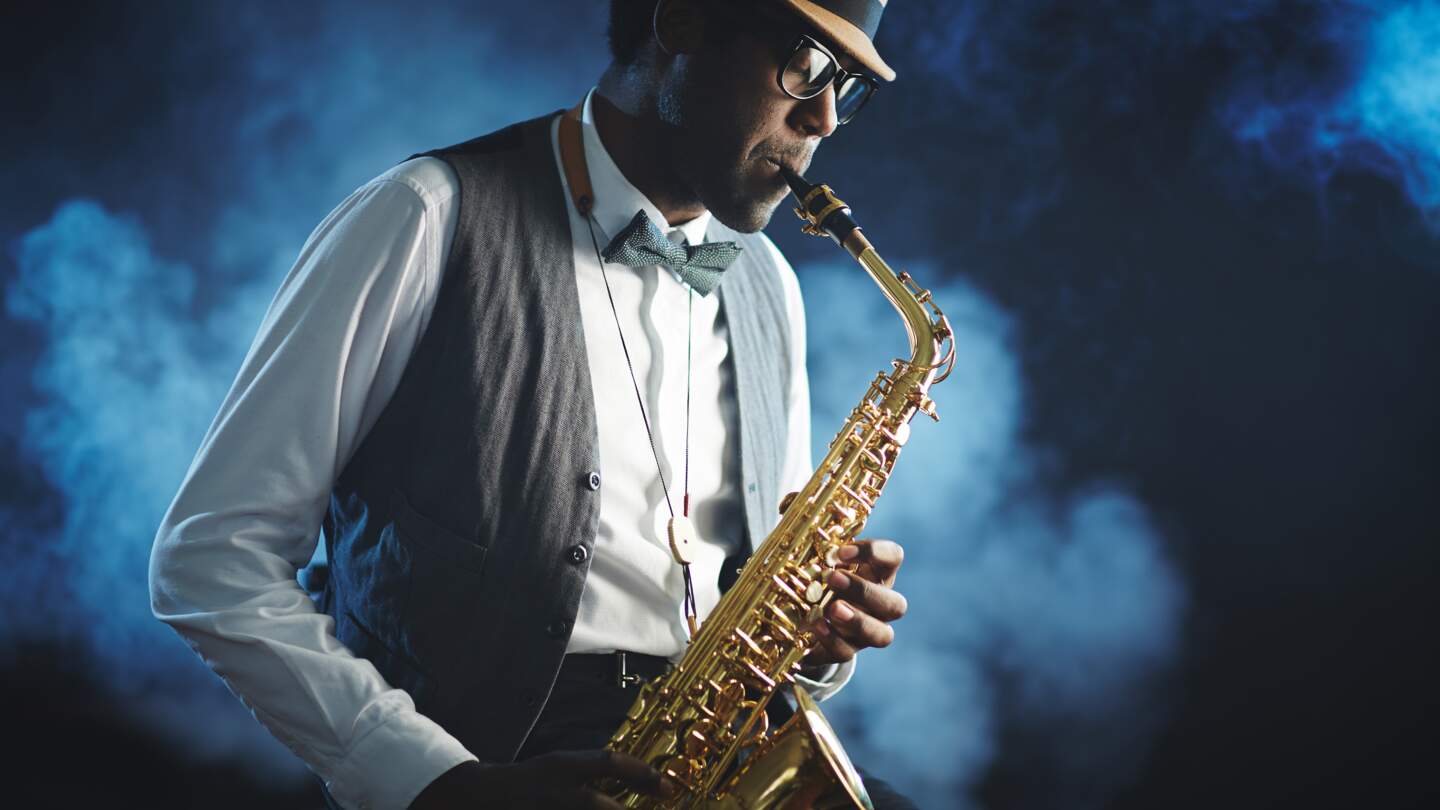 Mann spielt mit geschlossenen Augen Saxophon mit blauem nebligem Hintergrund | © Gettyimages.com/shironosov