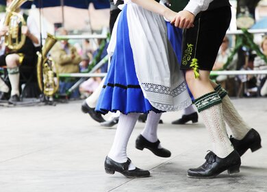 Junges bayerisches Paar in Lederhose und Dirndl tanzt zu typisch bayerischer Blasmusik | © Gettyimages.com/sebastian-julian