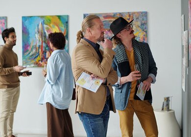 Menschen betrachten Gemälde an der Wand und diskutieren darüber, während sie die Ausstellung moderner Kunst in der Galerie besuchen | © Gettyimages.com/shironosov