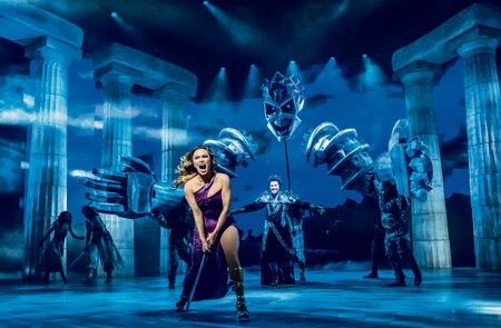 Meg von Disneys Hercules singend auf der Bühne, Hades mit spektakulärem Bühnenbild im Hintergrund | © Stage Entertainment/Johan Persson 