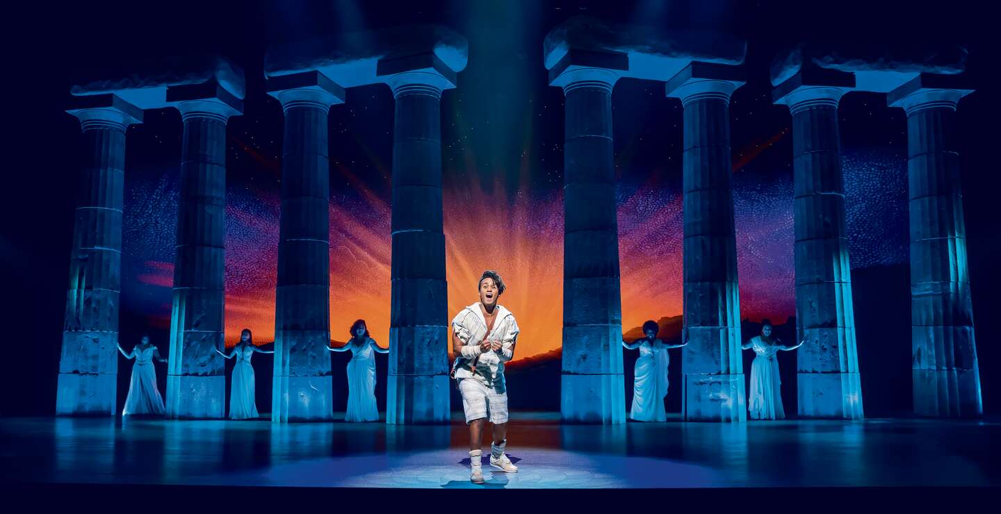 Disneys Hercules singt im Vordergrund, im Hintergrund sind Sänger in weißen Kleidern.  | © Stage Entertainment/Johan Persson 
