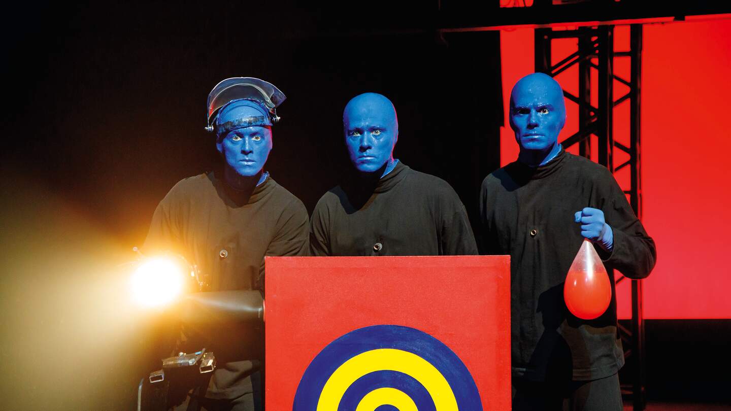 Blue Man Group hinter einer Zielscheibe, einer hält einen Ballon in der Hand | © Stage Entertainment/Morris Mac Matzen