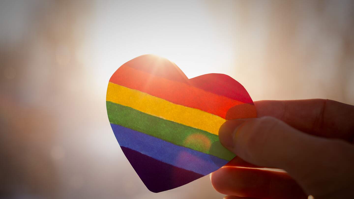 Hand hält ein Herz, das wie eine LGBT-Flagge gemalt ist und sich gegen die Sonne abhebt | © Gettyimages.com/Roman Didkivskyi