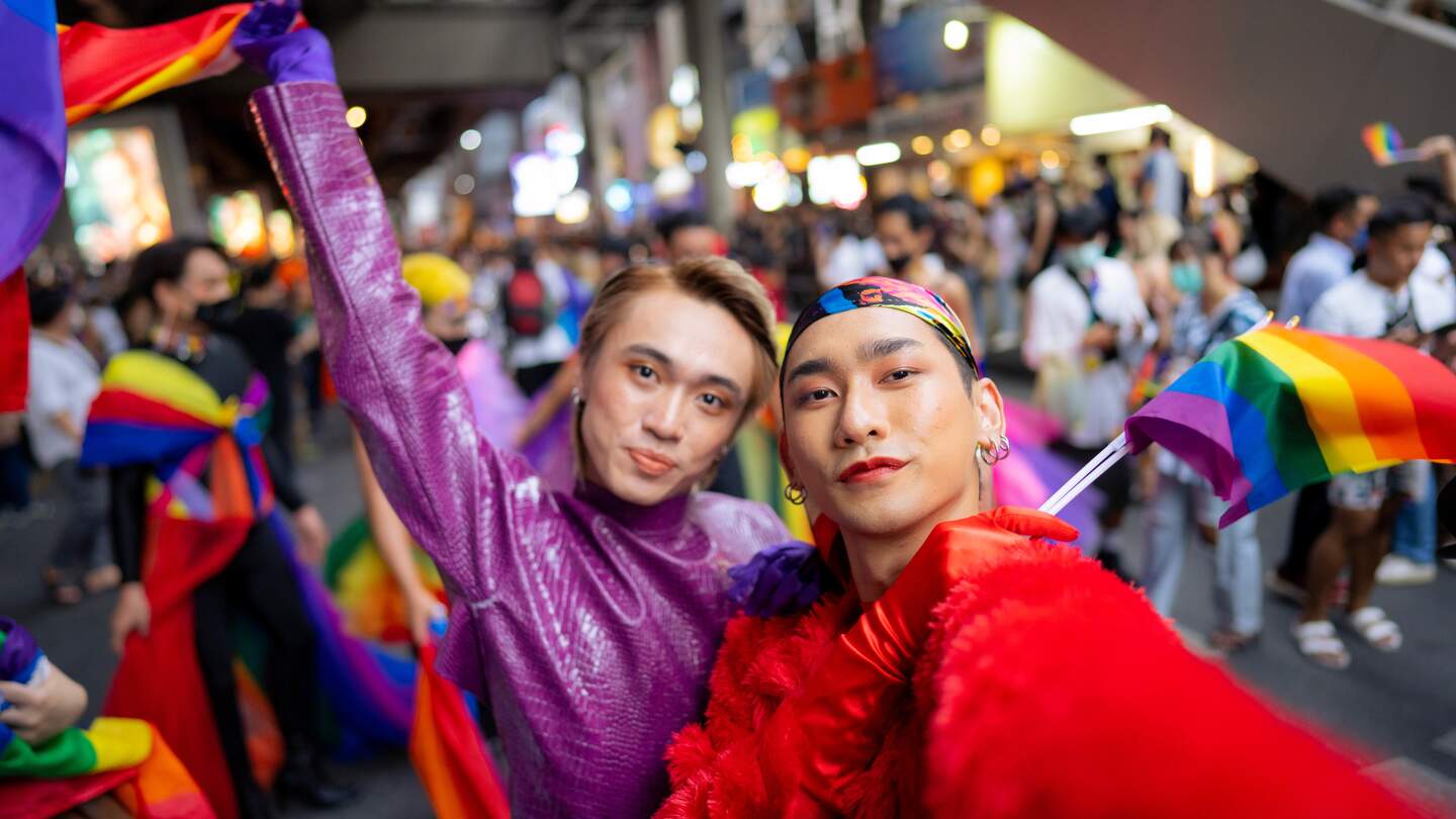 Schwules asiatisches Paar, das lächelt und ein Selfie macht, das die Pride-Parade genießt | © Gettyimages.com/whitebalance.oatt