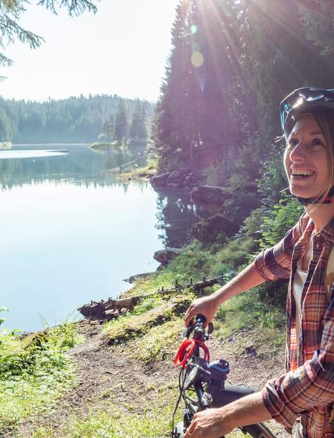 Frau auf dem Mountainbike mit Blick auf schönen Alpensee mit Sonnenschein | © GettyImages.com/Mystockimages