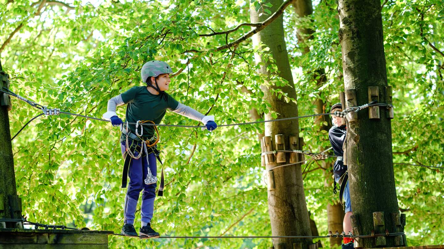 Zwei Kinder im Walderlebnispark, die gesicht und mit Helmen im Hochseilgarten klettern | © Gettyimages.com/romrodinka