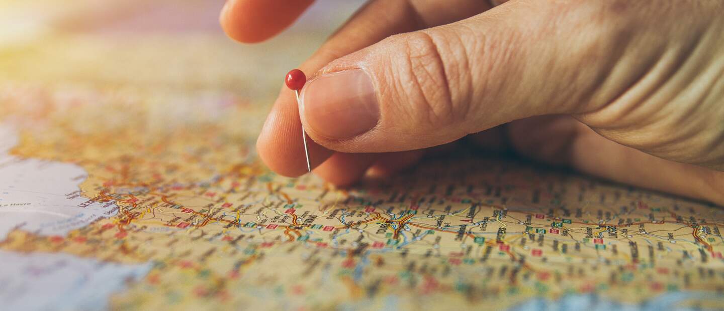Eine Hand ist dabei eine Stecknadel auf einer Weltkarte zu platzieren, um das nächste Reiseziel festzulegen | © Pixabay/piviso