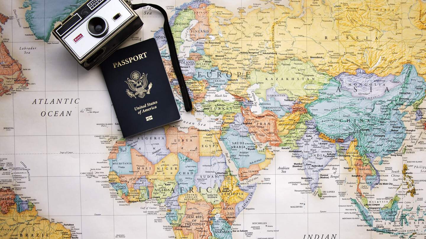 Auf einer bunten Weltkarte liegen ein altmodischer Fotapparat und ein Reisepass | © Pixabay/Pamjpat
