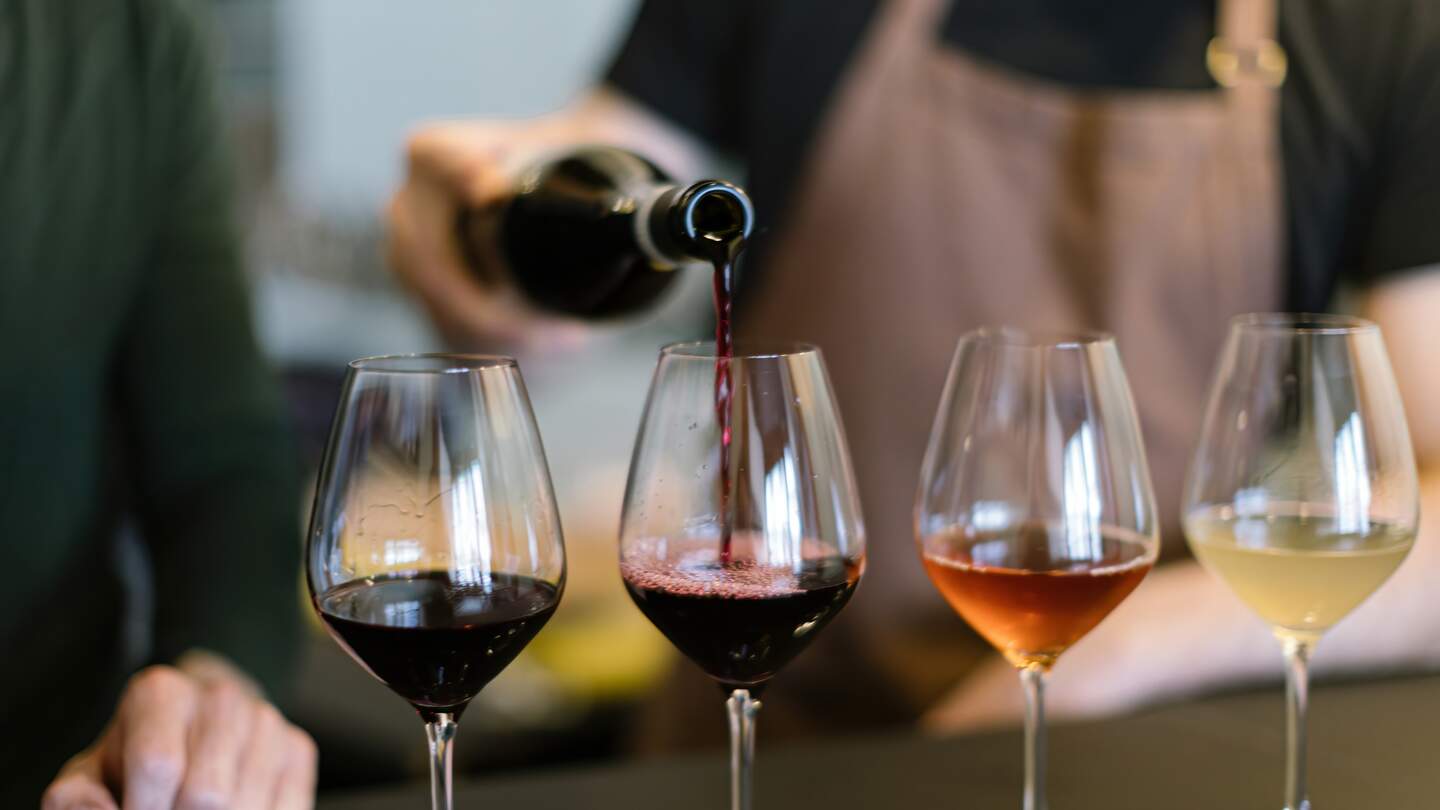 Einschenken verschiedener Weine in die Gläser, die für die Weinprobe auf der Theke arrangiert sind | © Gettyimages.com/Carlo Prearo