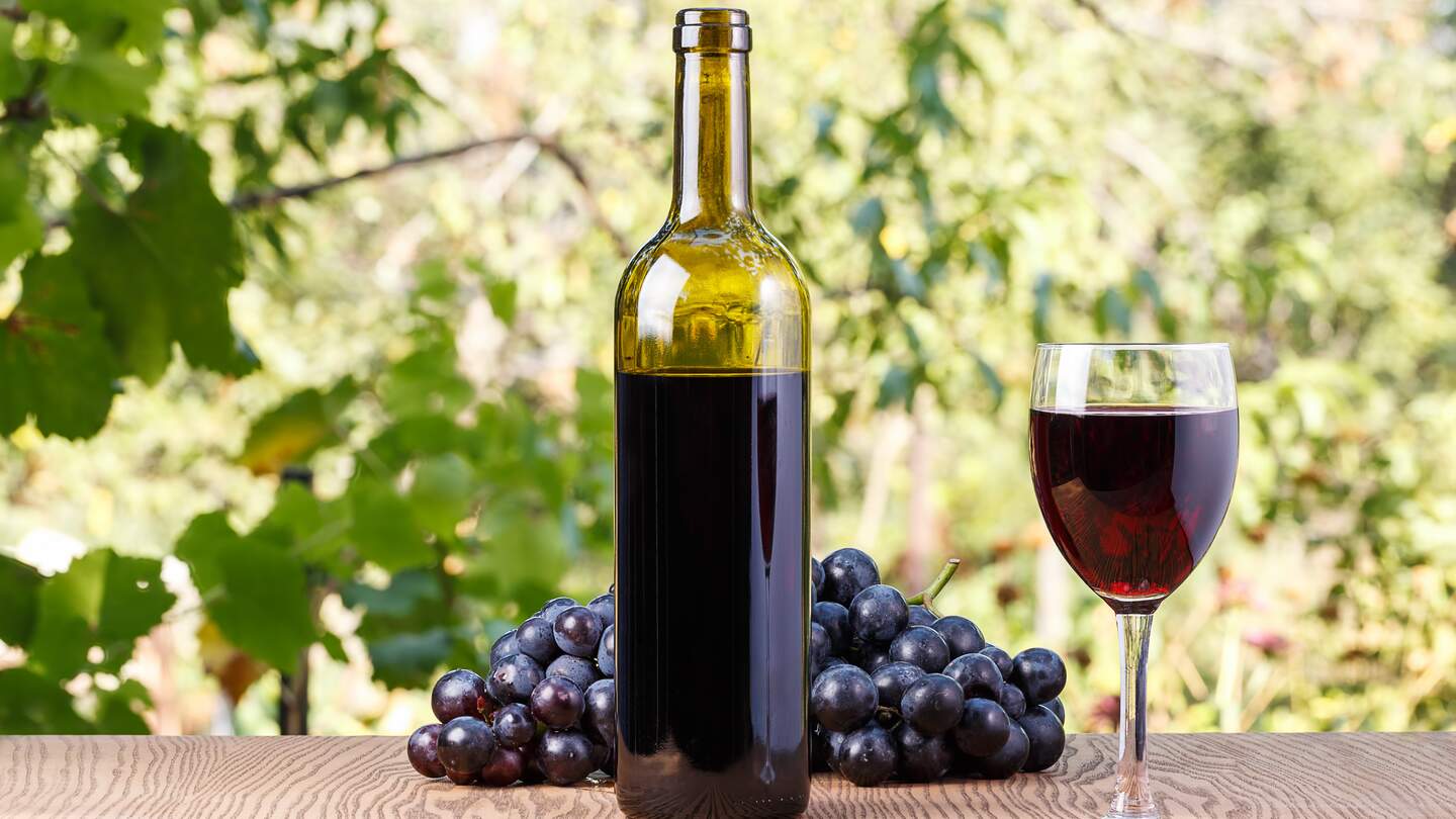 Flasche und ein Glas Wein mit Trauben auf einem hölzernen Hintergrund im Freien | © Gettyimages.com/baronvsp