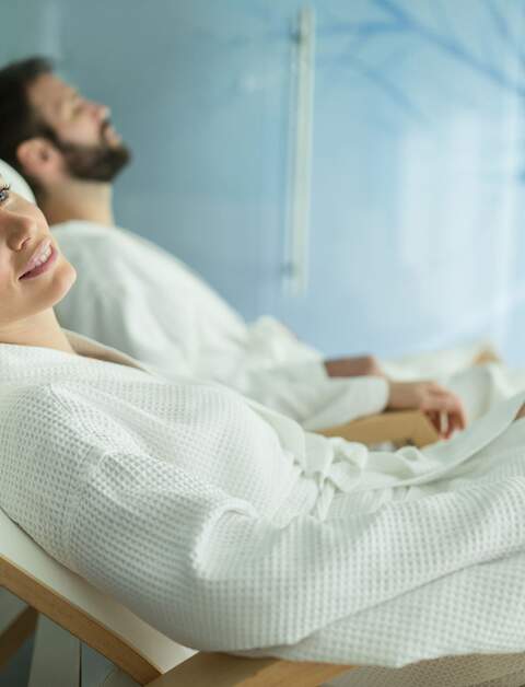 Frau und Mann in weißen Bademänteln entspannen auf Wellnessliegen | © Gettyimages.com/nd3000