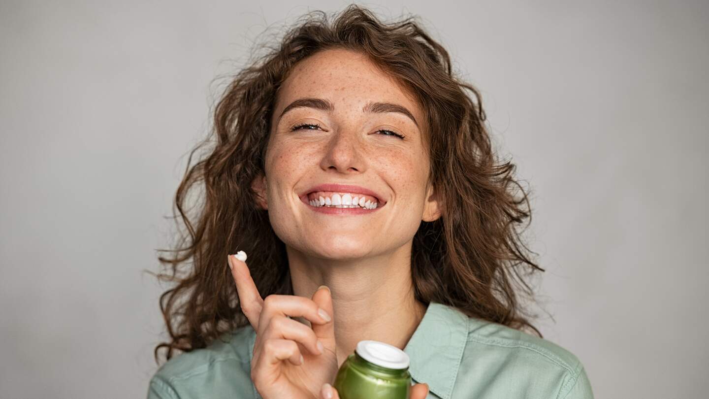 Schöne lächelnde Frau Anwendung Gesichtscreme aus grünem Glas | © Gettyimages.com/Ridofranz