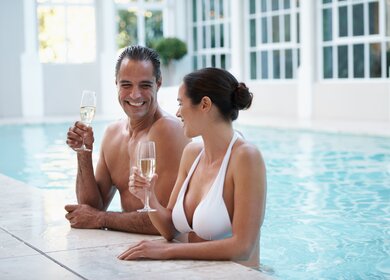 Beschnittene Aufnahme eines liebevollen Paares, das Champagner trinkt, während es sich in einem Pool entspannt | © Gettyimages.com/PeopleImages